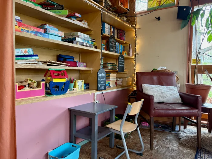 Play corner with kids desk and chair and shelves with toys and books next to a cozy leather chair and string lights