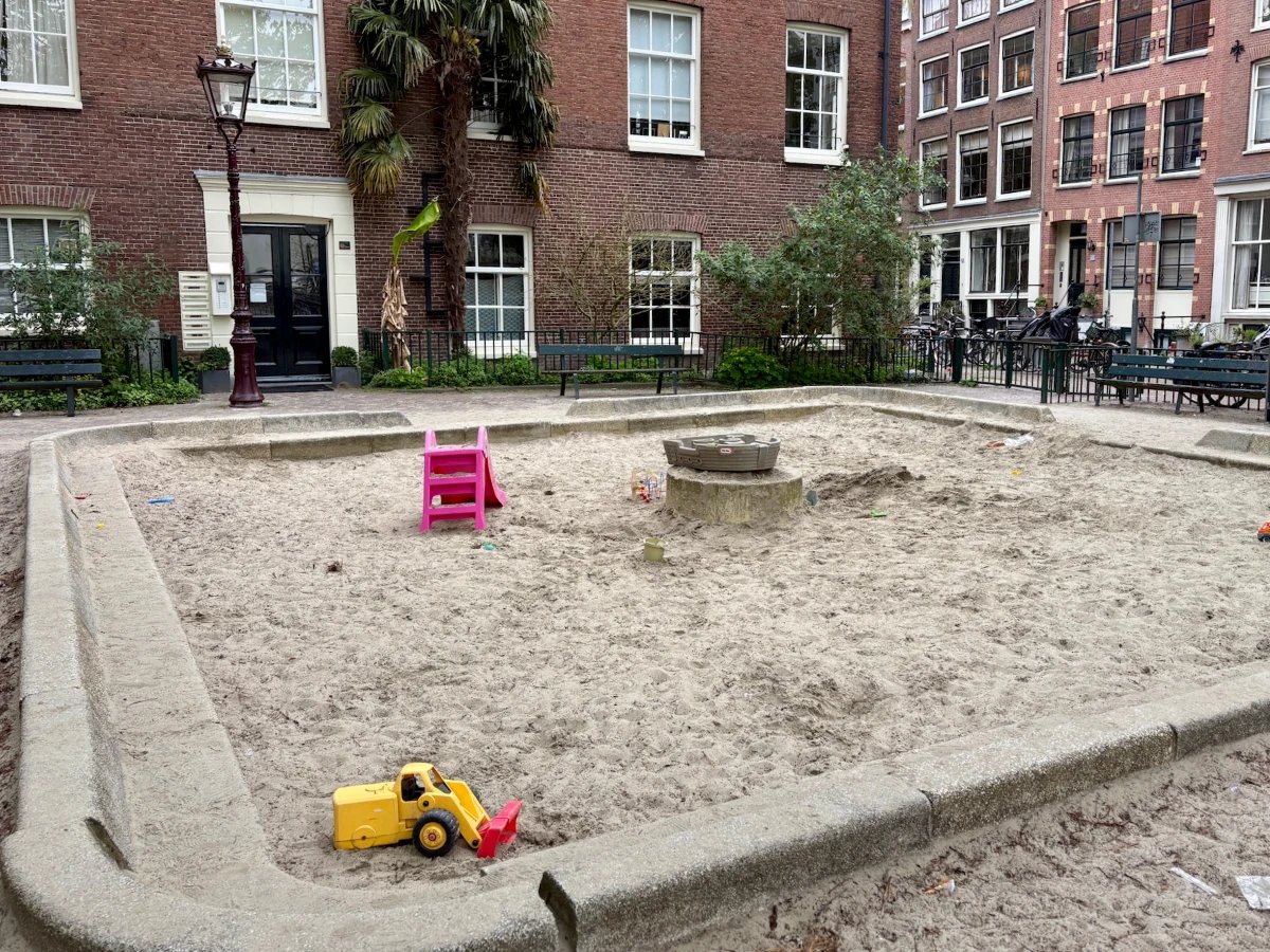 Large square sand box with a few toys surrounded by brick residential buildings