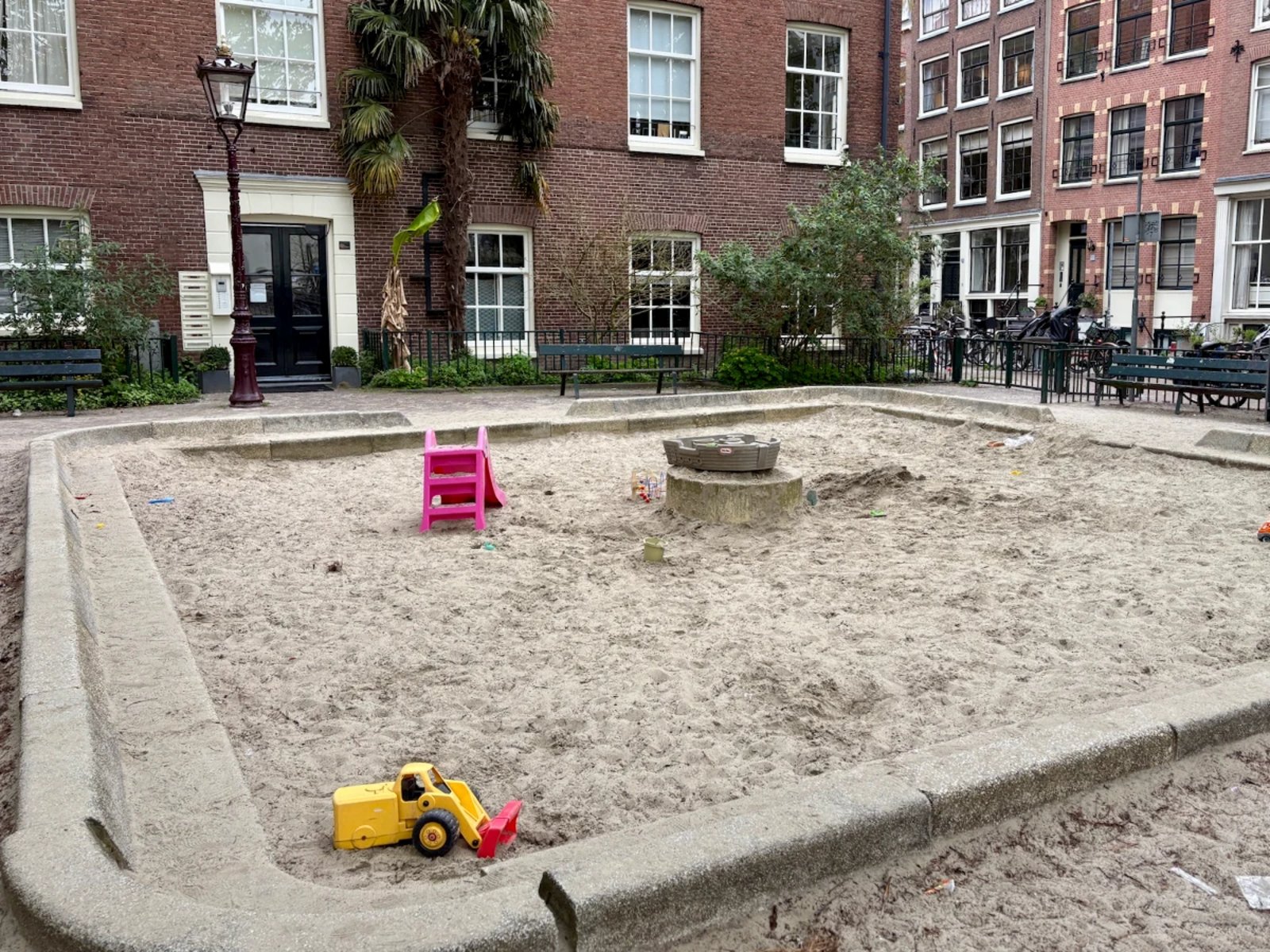 Large square sand box with a few toys surrounded by brick residential buildings