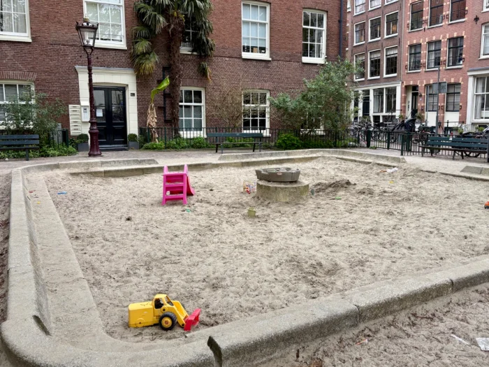 Large square sand box with a few toys surrounded by brick residential buildings