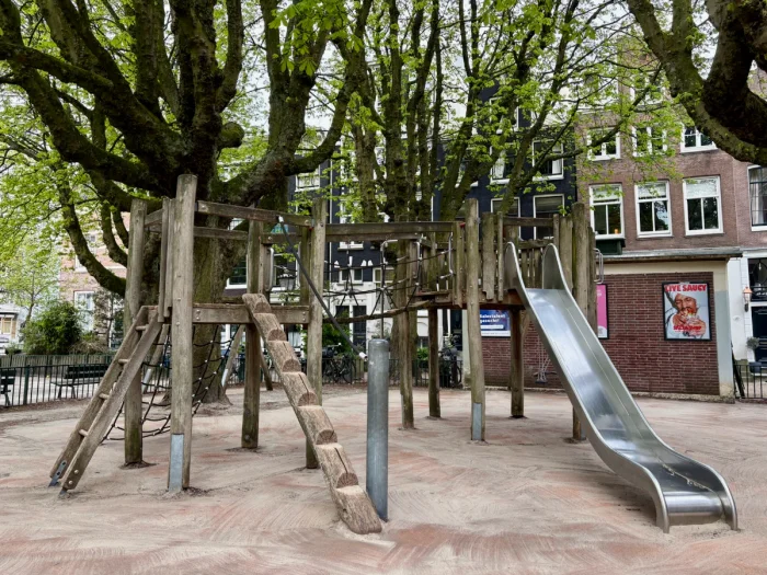 Wooden play structure with ladders, nets, and slide beneath massive trees