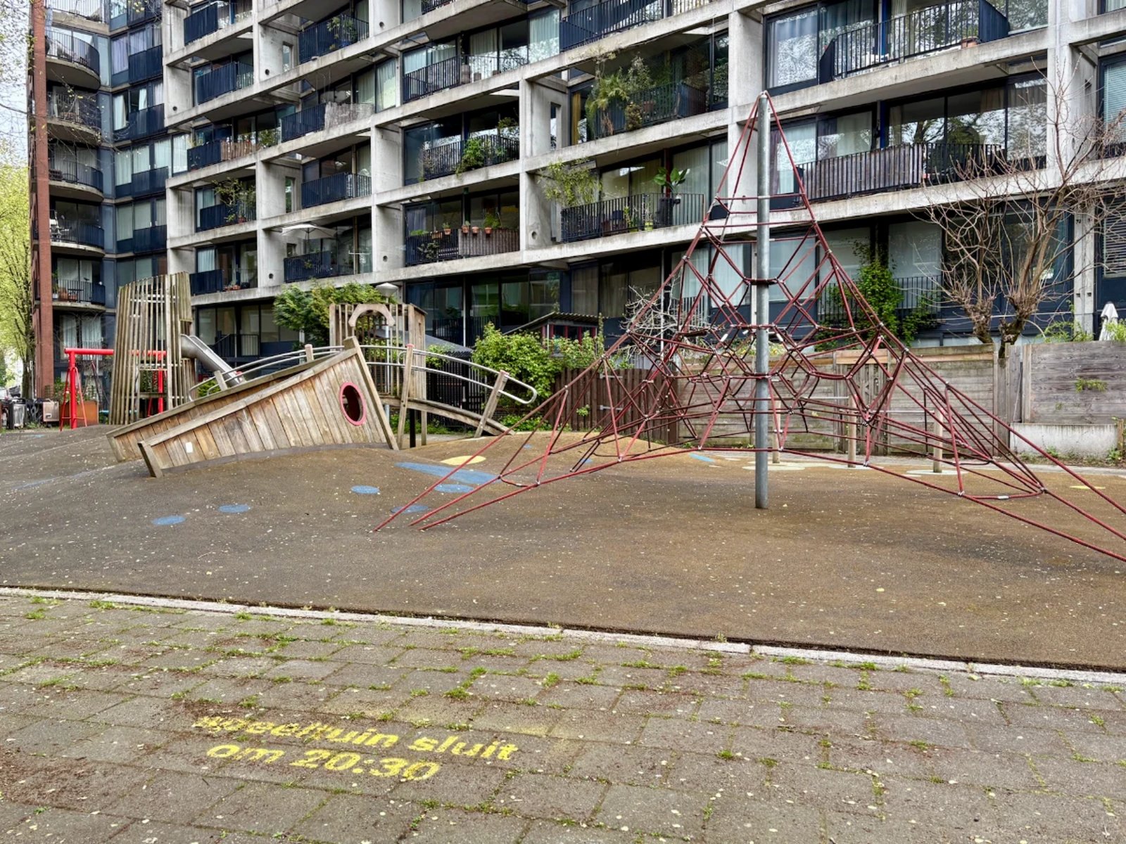 Playground next to modern residential building with wooden ship's hull and rope climbing pyramid