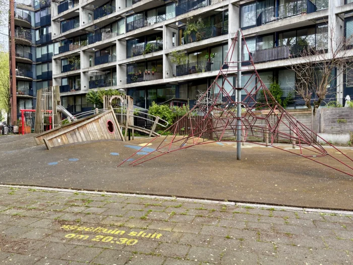 Playground next to modern residential building with wooden ship's hull and rope climbing pyramid