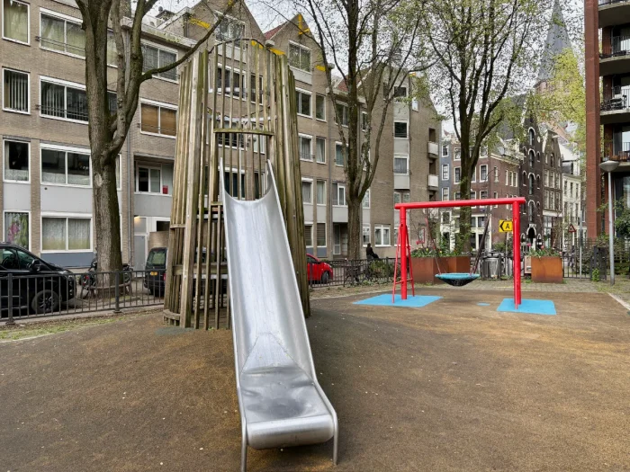 Tall wooden tower with slide next to red-frame nest swing set in shaded residential square