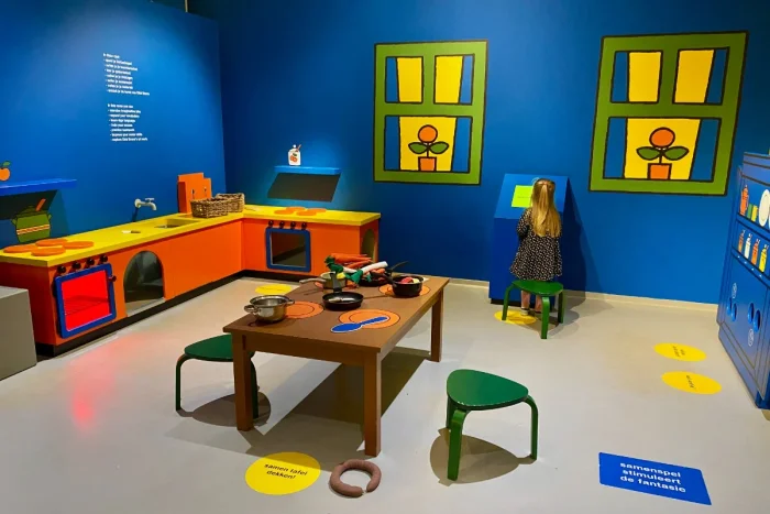 Girl plays in a play kitchen with bright blue walls and an orange and yellow kitchen