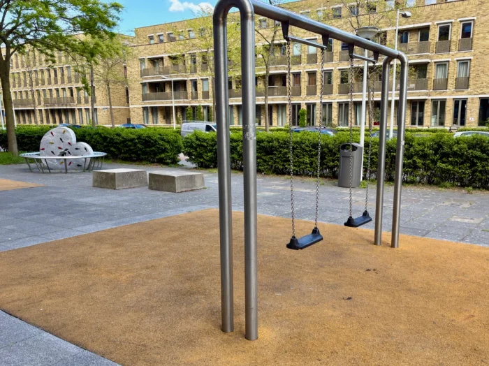 Modern metal frame swing set with two swings and benches and residential buildings behind