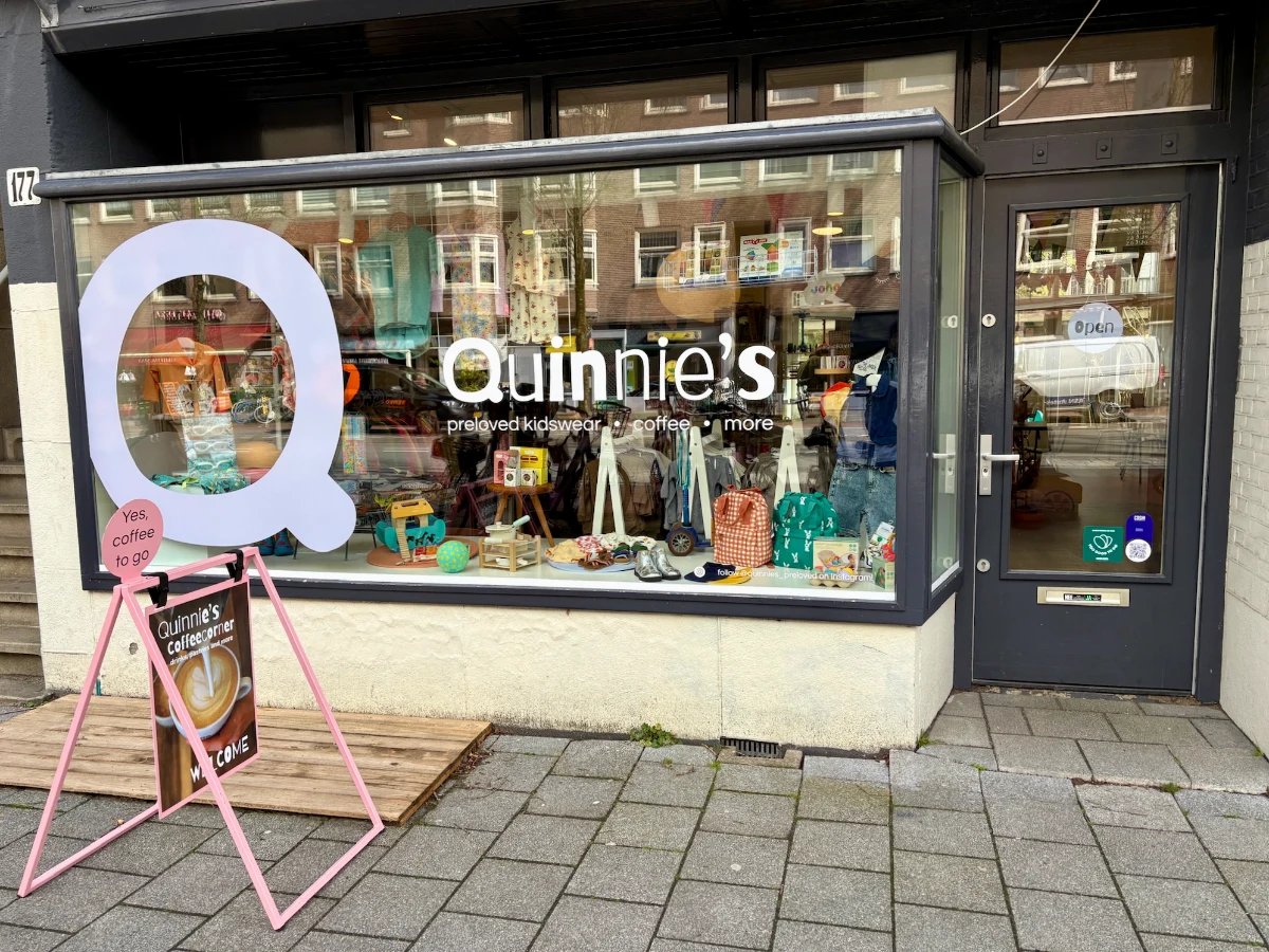 Entrance and storefront for Quinnie's with toys and clothing on display int he window and big Q on the glass
