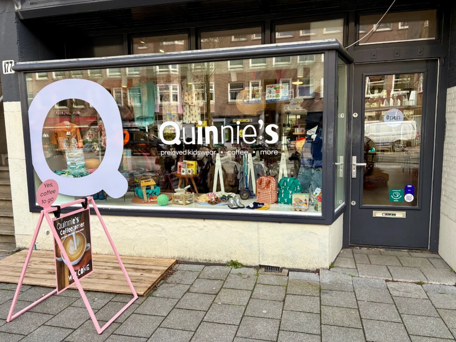 Entrance and storefront for Quinnie's with toys and clothing on display int he window and big Q on the glass