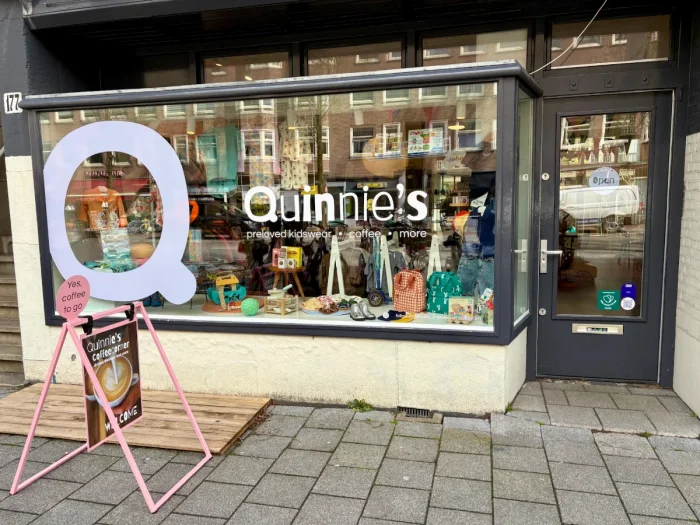 Entrance and storefront for Quinnie's with toys and clothing on display int he window and big Q on the glass