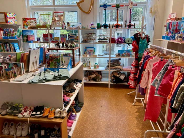 Second hand kids clothing shop with racks of clothes, shelves of shoes, and a variety of toys on the back wall
