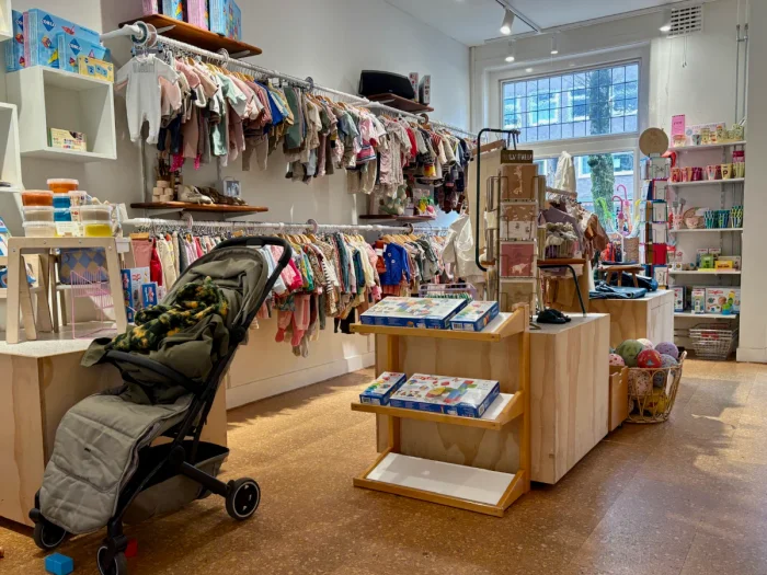 Stroller parked in kids clothing shop with rack of tiny clothes on the wall and toys on display
