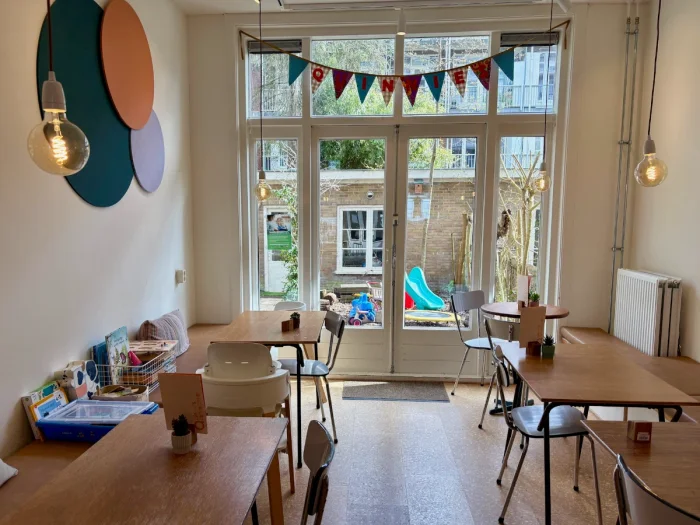 Small kid cafe seating area with banner and colorful circles on the wall and glass doors leading to small garden