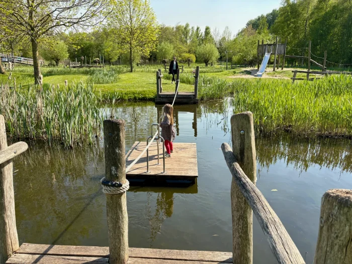 Young girl using hand-operated ferry moving across a canal with tall grass and sunny lawn on other side