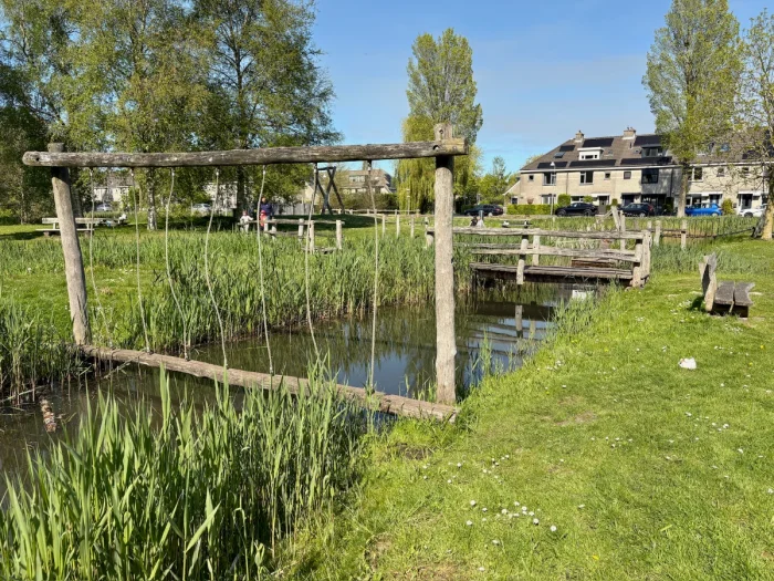 Balance beam and rustic wooden bridge spanning a canal with tall grasses and trees surrounding