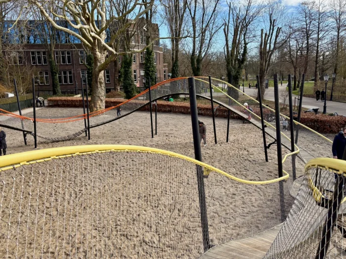 Elevated undulating walkway with yellow and red railing and mesh with sand below