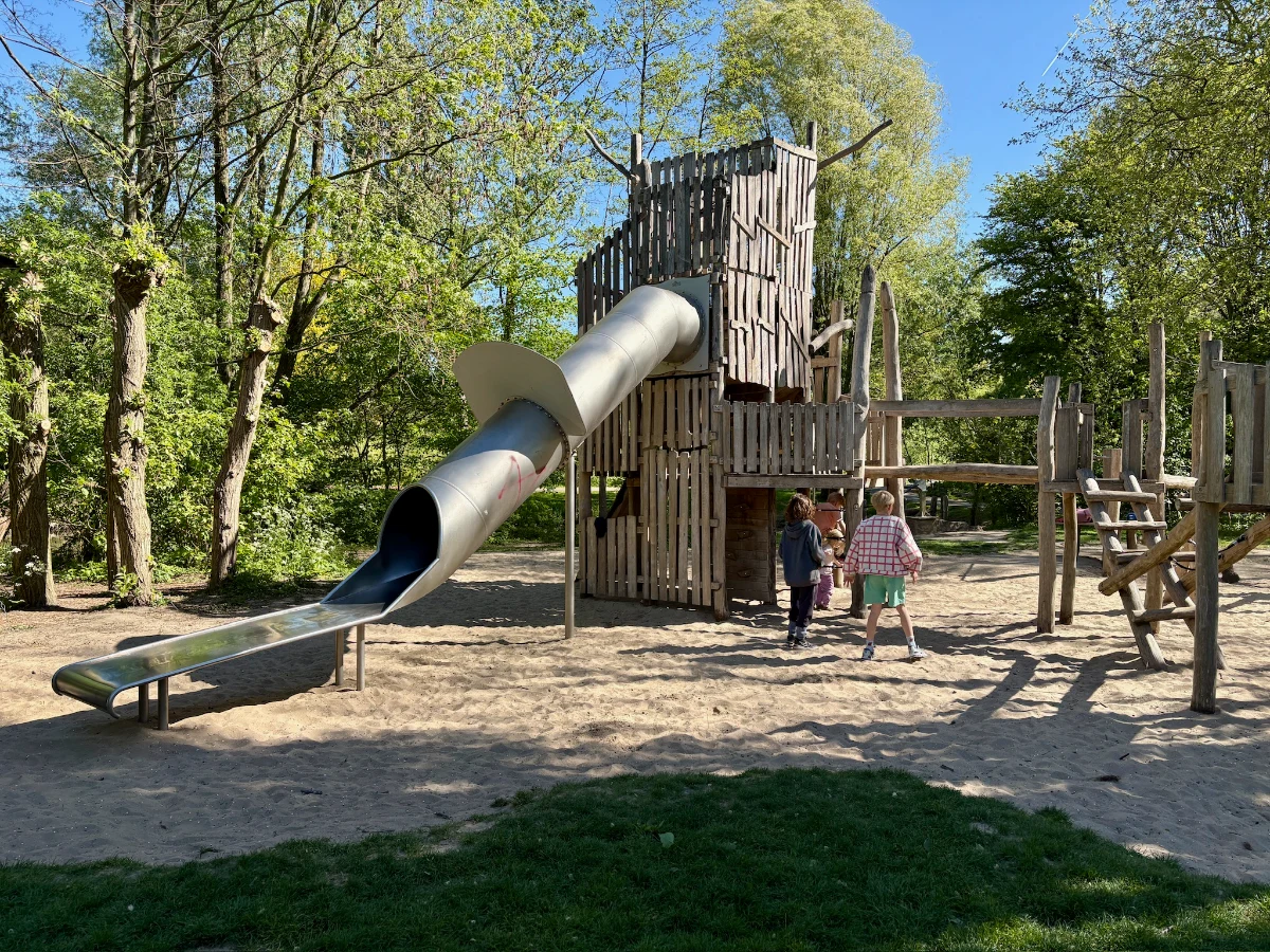 Tall wooden tower with enclosed slide set on sand in park setting