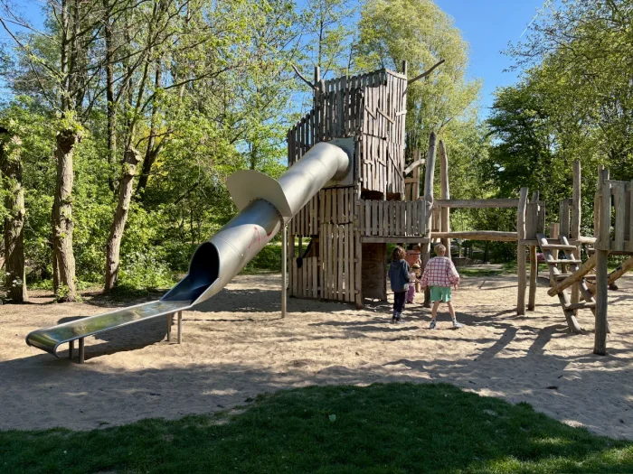 Tall wooden tower with enclosed slide set on sand in park setting