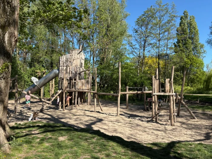 Natural wood climbing structure and obstacle course with slide and trees around
