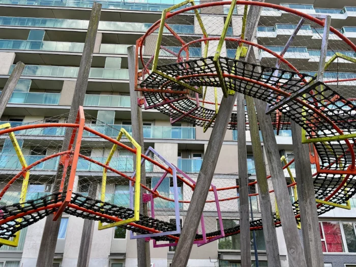 Looking up at modern steel and rope curvy play structure on stilts with modern high rise condos behind