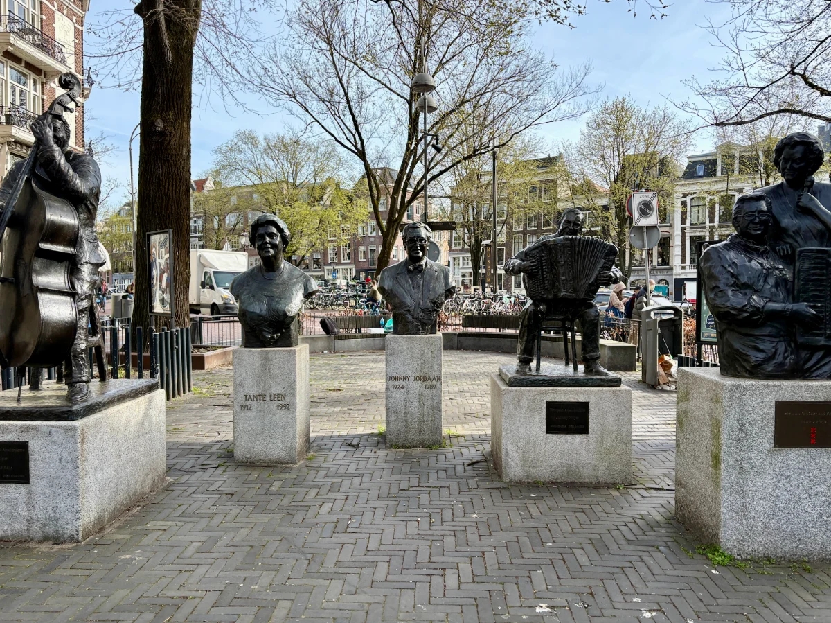 Statues and busts of famous Dutch musicians and singers in a sunny Amsterdam square with canal houses behind