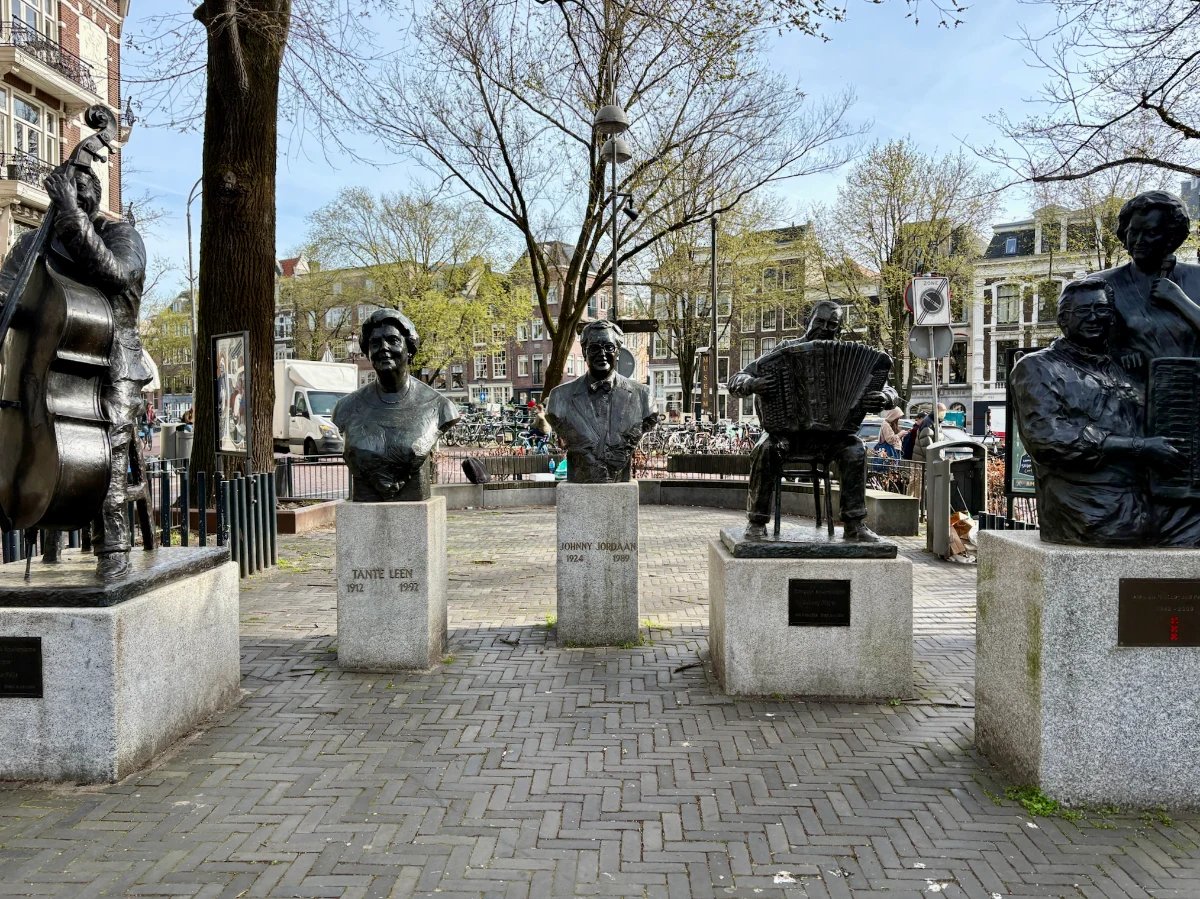 Statues and busts of famous Dutch musicians and singers in a sunny Amsterdam square with canal houses behind