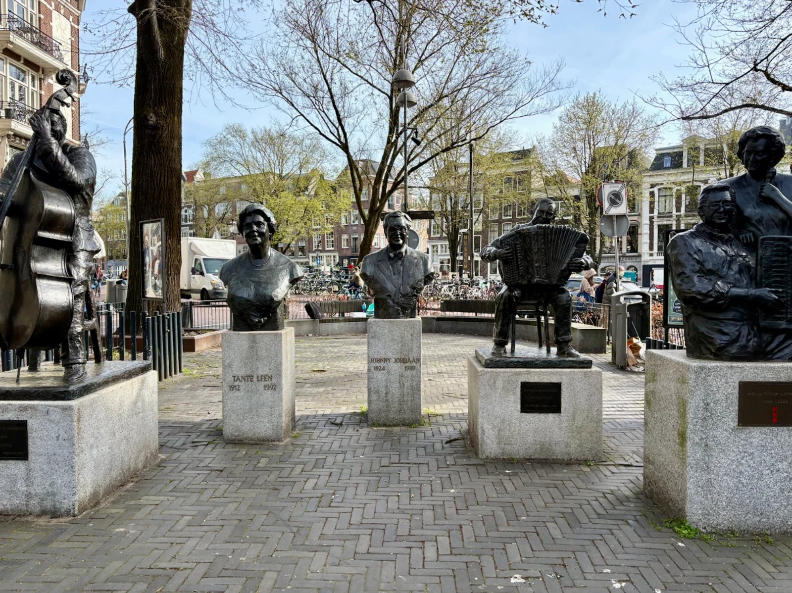Statues and busts of famous Dutch musicians and singers in a sunny Amsterdam square with canal houses behind