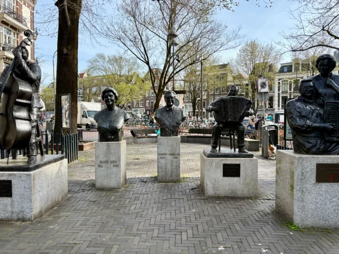 Statues and busts of famous Dutch musicians and singers in a sunny Amsterdam square with canal houses behind