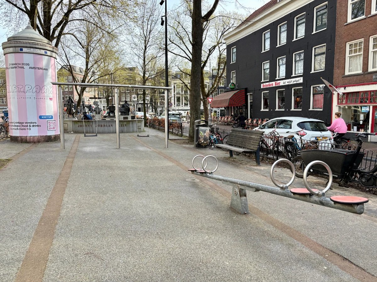 Metal seesaw and swing set on concrete with buildings, cars, and a pink and white striped advertisement on a peperbus