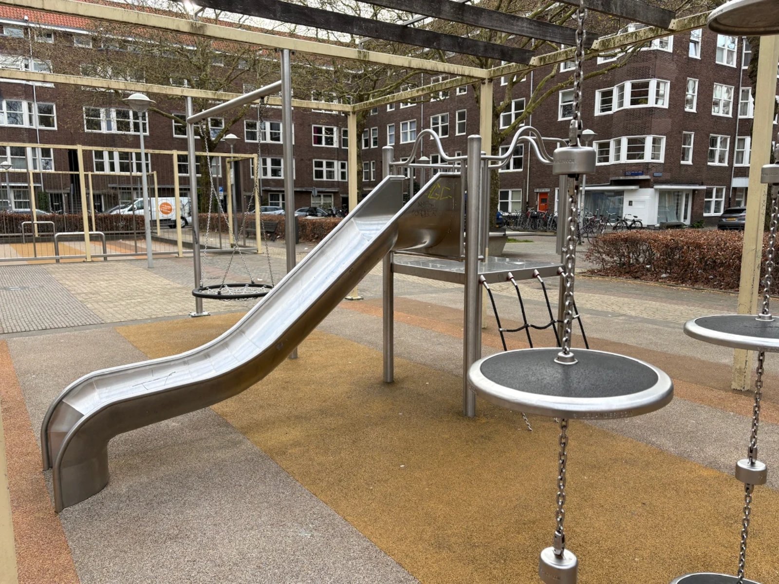 Metal slide, balance discs, and nest swing on yellow and orange striped playground with yellow frame overhead