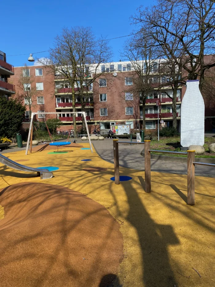 Children's playground with yellow ground, slide, nest swing and large milk bottle outdoor artwork