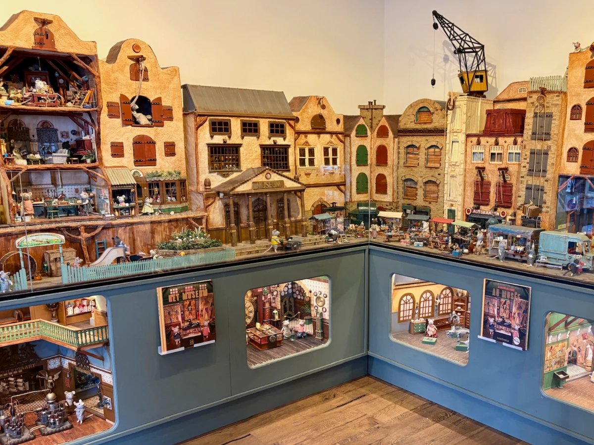 Display of miniature mouse-sized world with canal houses and display cases beneath showing inside of buildings