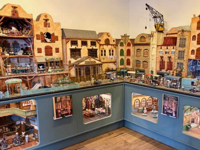 Display of miniature mouse-sized world with canal houses and display cases beneath showing inside of buildings