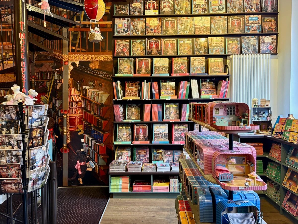 Colorful store with floor to ceiling bookshelves, a postcard rack, and small lunchbox-sized dollhouses on display