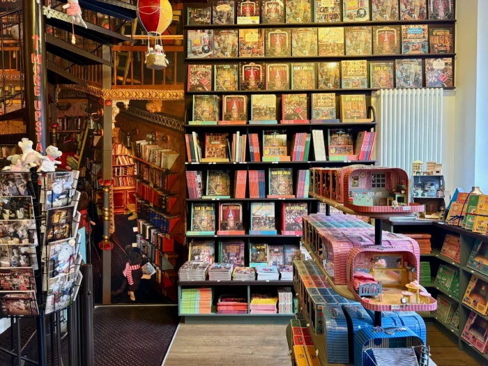 Colorful store with floor to ceiling bookshelves, a postcard rack, and small lunchbox-sized dollhouses on display