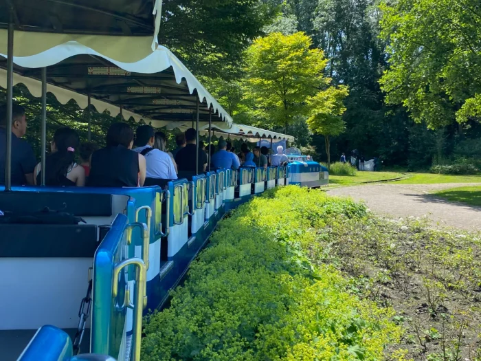 People riding on a blue and white open-air train through a green park