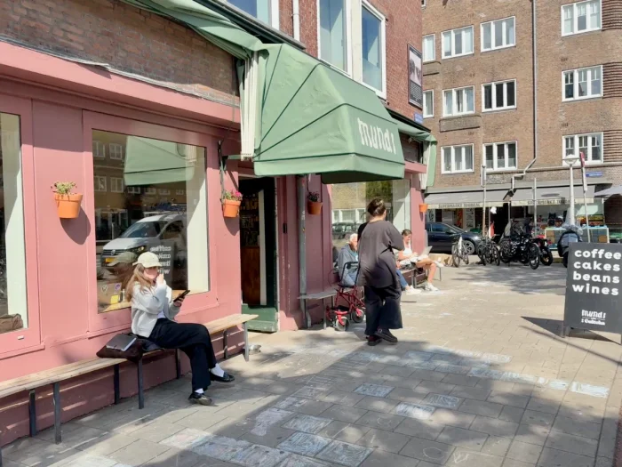 People outside coffee shop with green awning and sandwich board