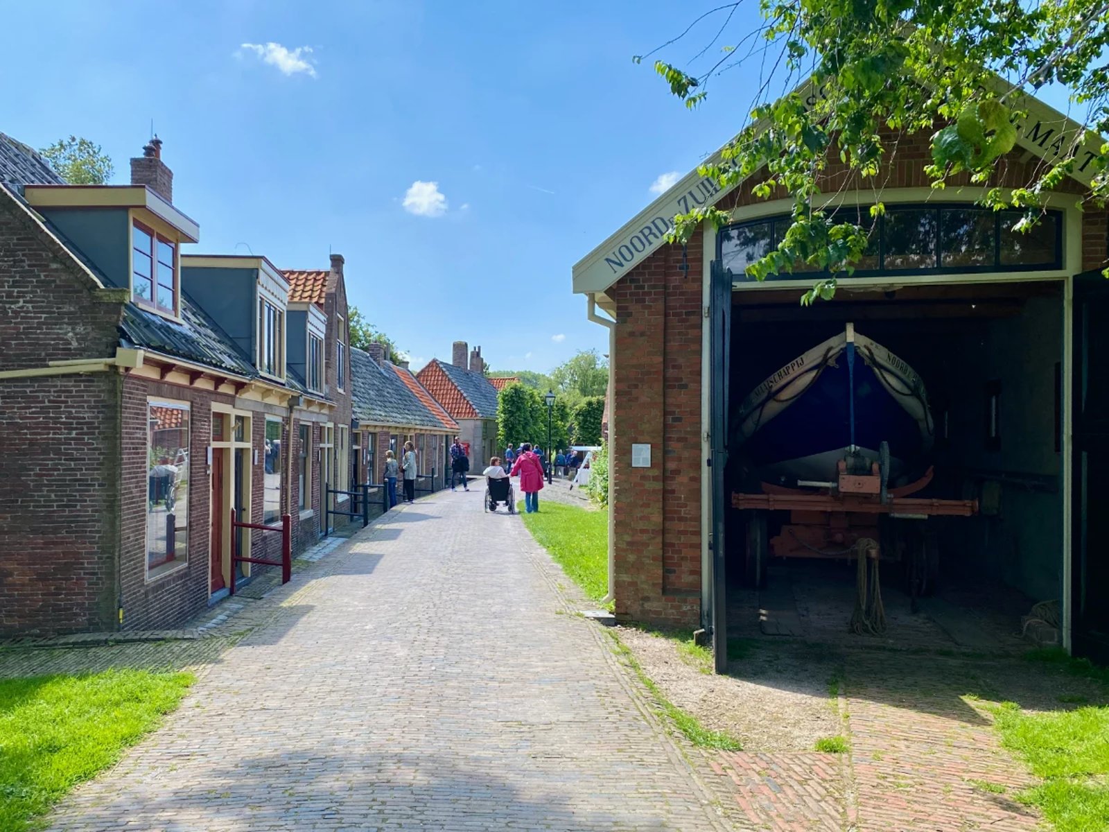 People walking down a quaint street with historic homes and a shed with boats