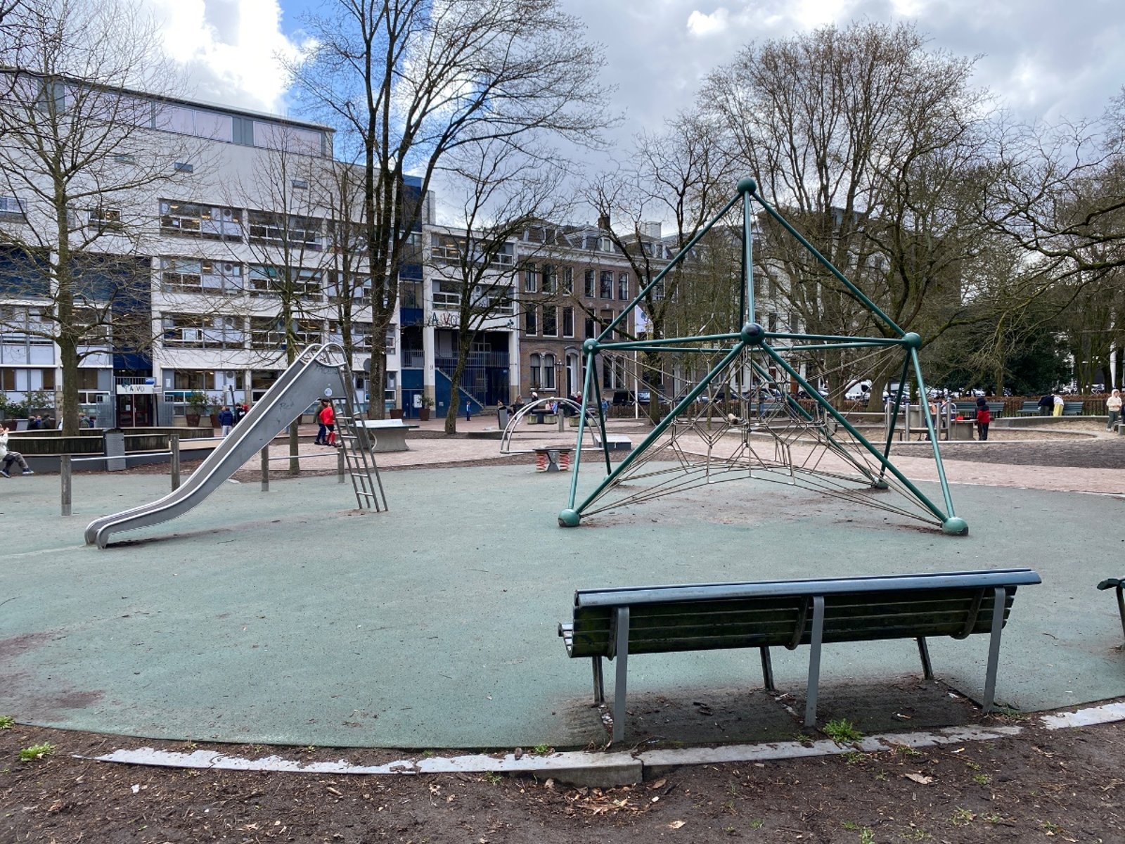 A playground with a slide, modern metal climbing structure and bench in the foreground