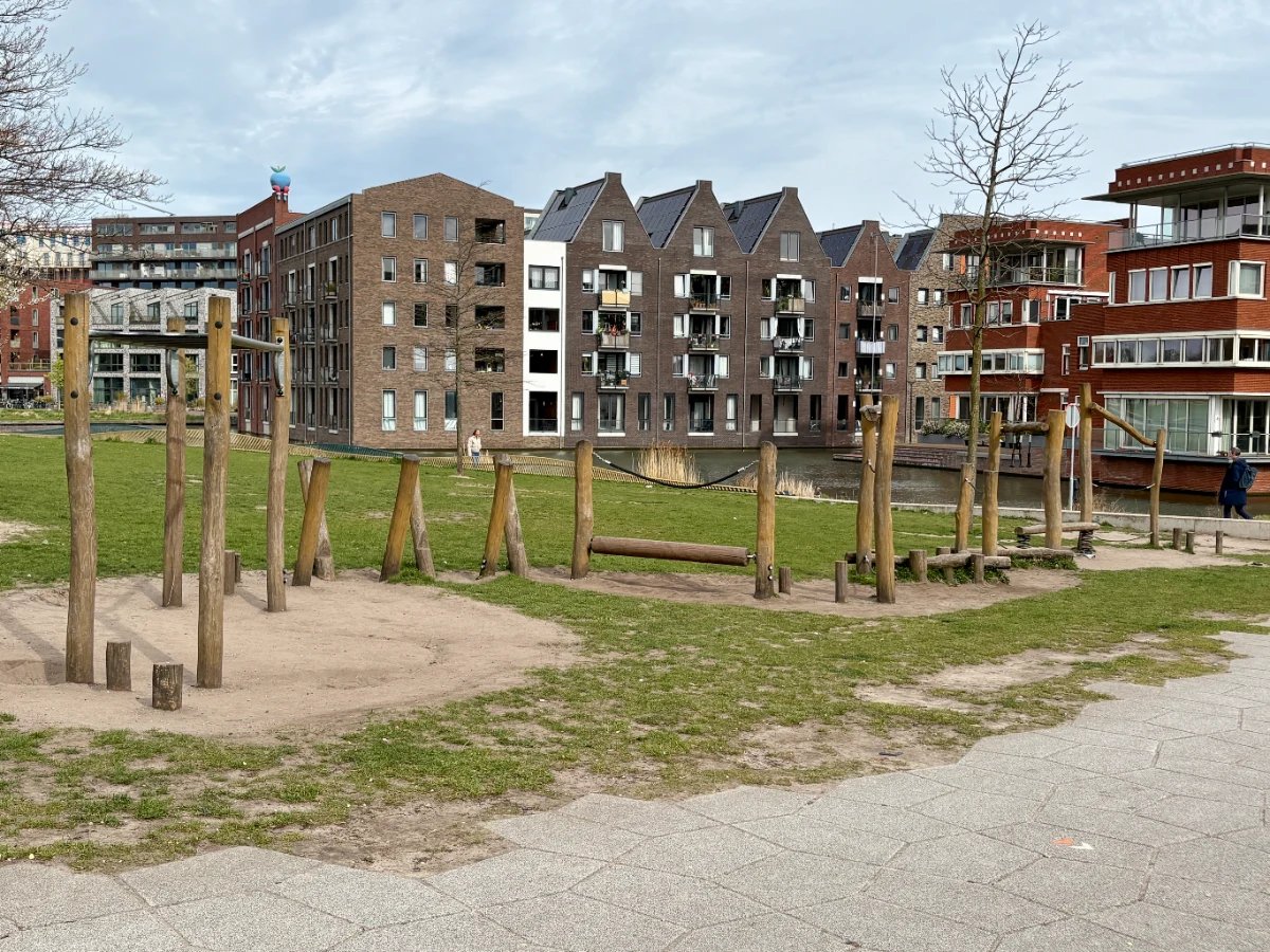 Natural obstacle and balance course on grassy lawn with Dutch houses and canals behind