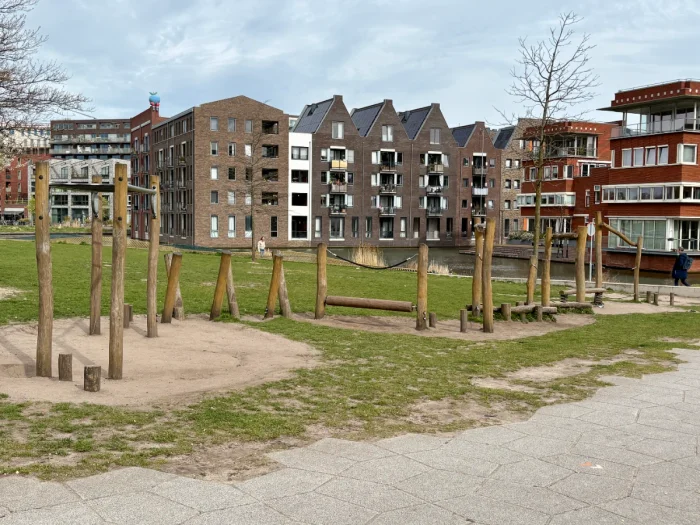 Natural obstacle and balance course on grassy lawn with Dutch houses and canals behind