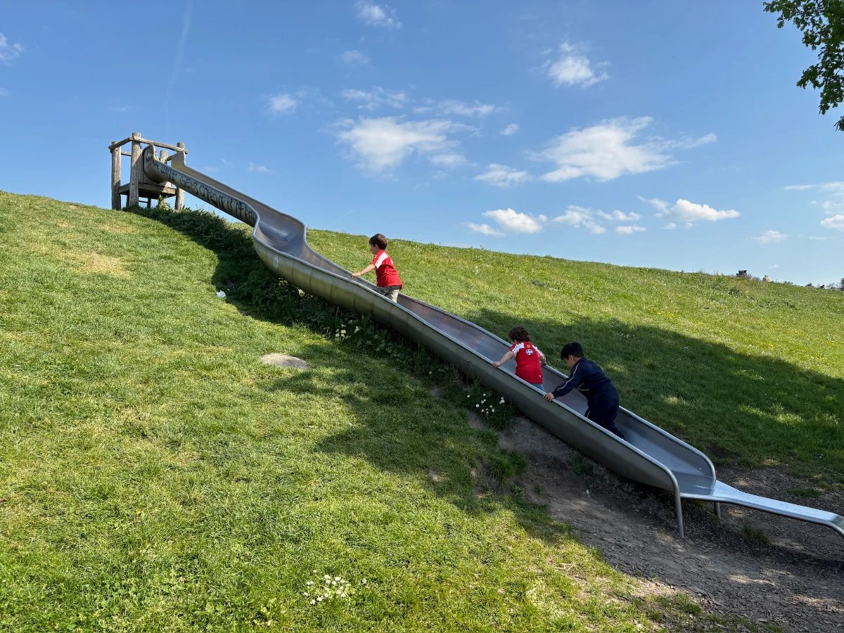 Kids climbing up a long metal slide built into a hillside