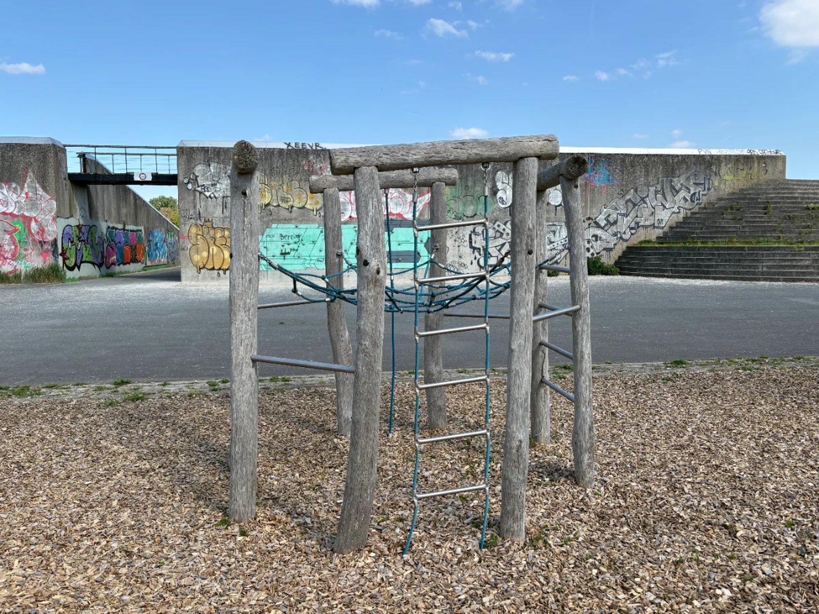 Wood and rope climbing structure with grafitti-covered wall and staircase behind